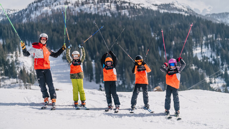 Grupa narciarzy, w tym dzieci, radośnie pozuje na stoku.