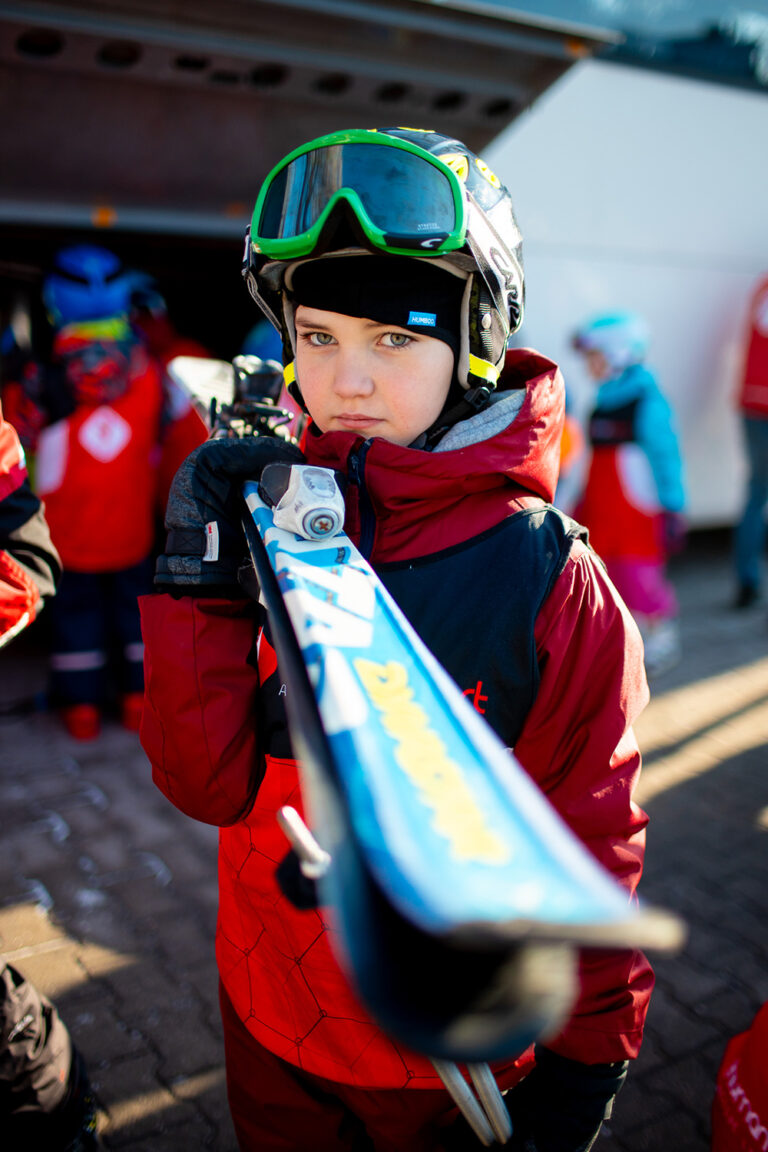 Dziecko w kasku i goglach narciarskich trzyma narty.