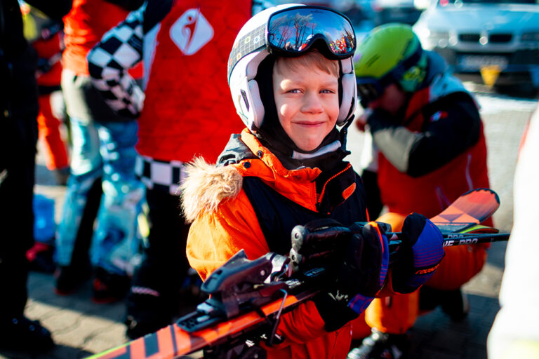 Uśmiechnięty chłopiec w narciarskim stroju z nartami i kijami.