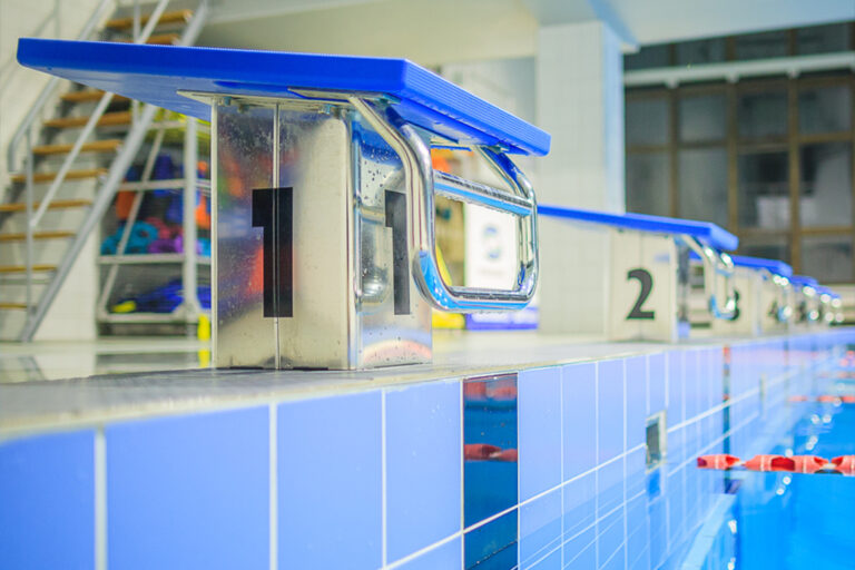 Basen pływacki z niebieskimi słupkami startowymi i numerami torów. Idealne miejsce do treningów.