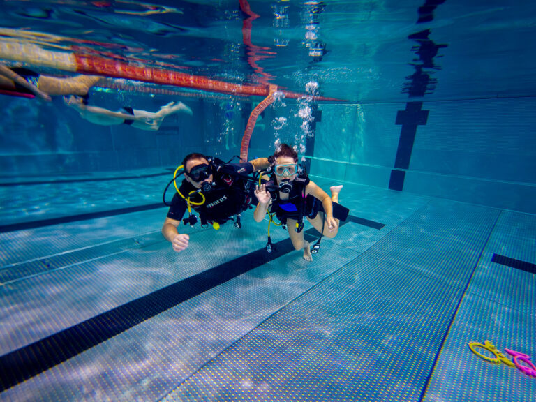 Para nurków pod wodą w basenie. Nauka nurkowania, podwodna przygoda.