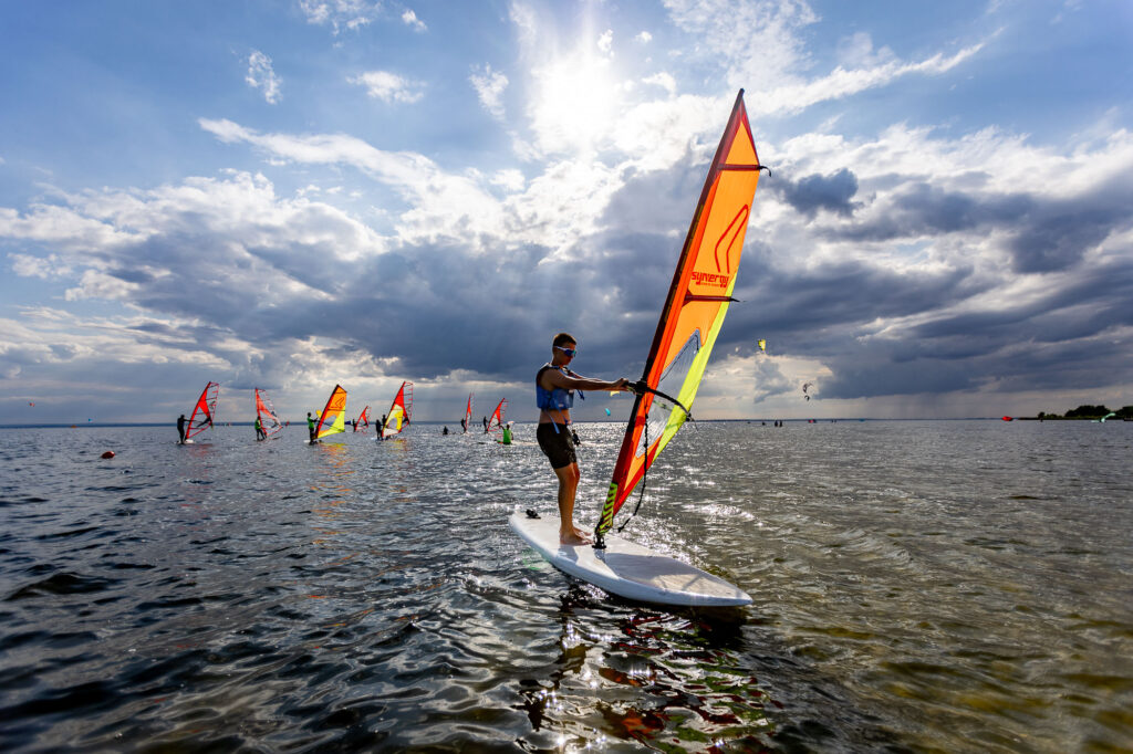 Windsurfingista na desce z czerwono-żółtym żaglem na wodzie