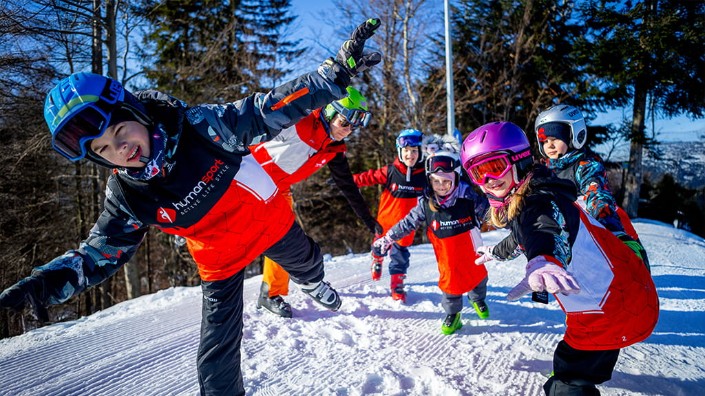 Dzieci w kaskach narciarskich i czerwonych kurtkach HumanSport bawią się na stoku podczas ferii zimowych 2026 w Beskidach, nauka jazdy na nartach dla dzieci.